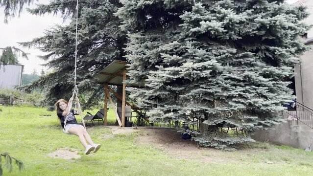 Teenage girl is playing on swing, dream fly. Young girl is swinging in the yard under the tree, beautiful nature. 15 years old girl in flight. Family, dream entertainment, relaxing concept