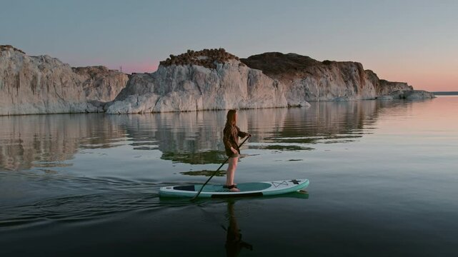 Close up video of young surfer lady is walking on standup paddle sup board at calm sunset lake