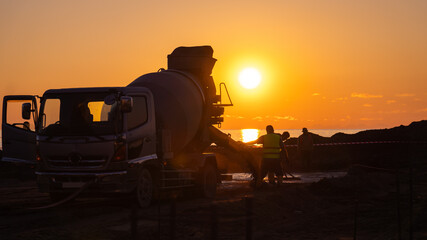 Close-up at sunset on the seashore of a concrete mixer truck with people in work uniforms. Concept...