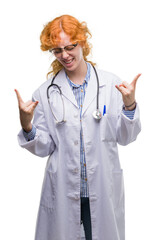 Young redhead woman wearing doctor uniform shouting with crazy expression doing rock symbol with hands up. Music star. Heavy concept.