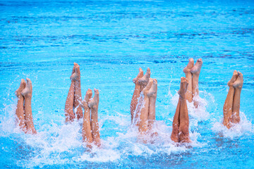 Artistic swimming team performing synchronized legs movement in swimming pool with copy space
