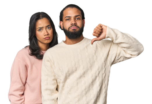 Young Latino couple in studio showing a dislike gesture, thumbs down. Disagreement concept.