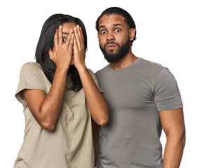 Young Latino couple in studio blink through fingers frightened and nervous.