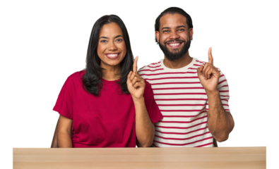 Seated young Latino couple at table showing number one with finger.