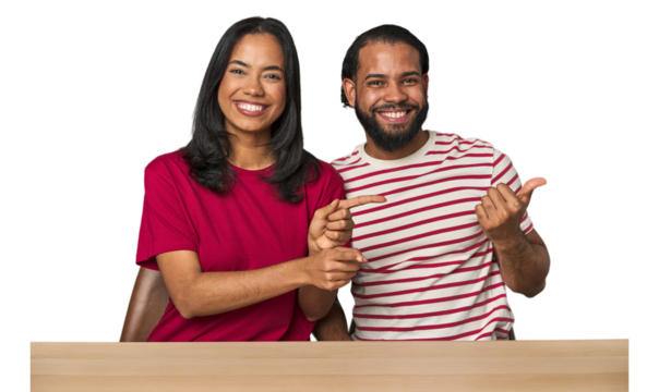 Seated young Latino couple at table excited pointing with forefingers away.