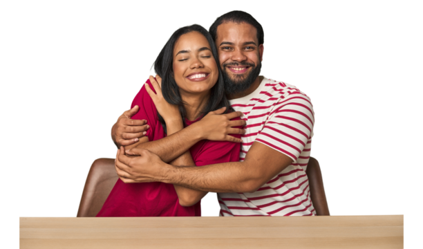 Seated young Latino couple at table hugs, smiling carefree and happy.