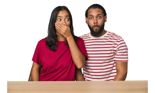 Seated young Latino couple at table thoughtful looking to a copy space covering mouth with hand. - Powered by Adobe