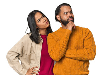 Young Latino couple in studio thinking and looking up, being reflective, contemplating, having a...