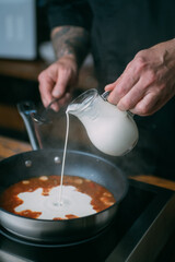 Cooking sauce in a frying pan. Close-up. Male chef's hands mix cream and tomato sauce