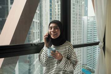 Fototapeta premium A woman is smiling and holding a cup of coffee while holding a cell phone. Concept of relaxation and enjoyment, as the woman is taking a break from her daily routine to enjoy a warm beverage