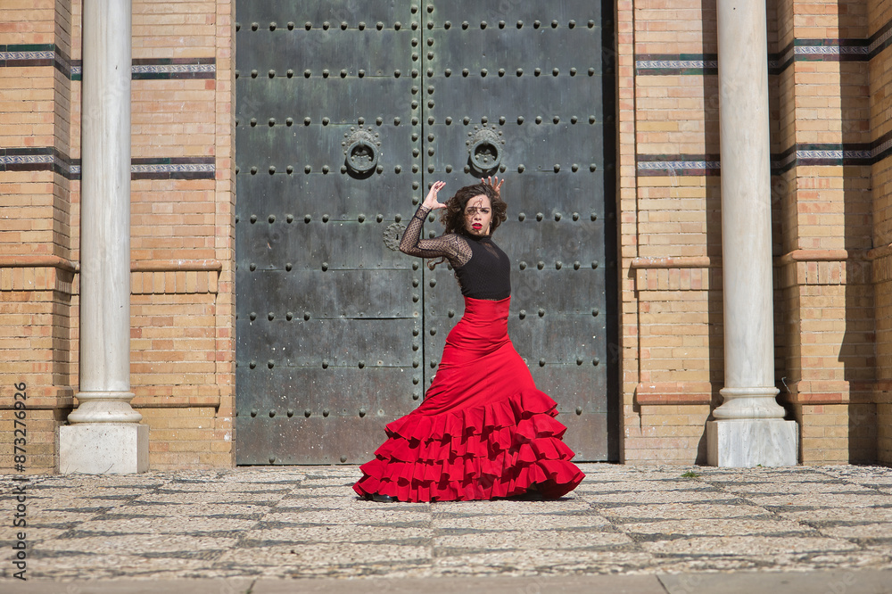 Wall mural Young, beautiful, brunette woman in black shirt and red skirt, dancing flamenco in front of an old, black metal door. Flamenco concept, dance, art, typical Spanish.