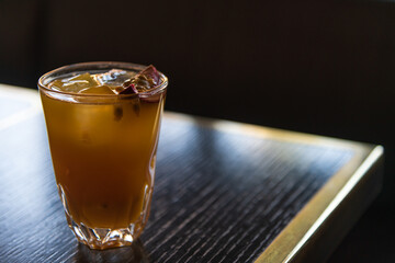Close-up view of orange lemonade in drinking glass standing on wooden table in cafe. Copy space for your text. Ice cubes and piece of passion fruit floats on top of cold drink. Summer drinks theme.