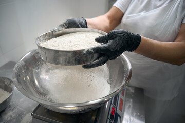 Worker in overalls sifts flour into a bowl