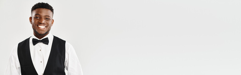 A young African American groom, looking handsome in a tuxedo, smiles warmly at the camera in a studio setting against a grey background.