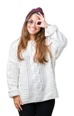 Young beautiful brunette hipster woman wearing sunglasses over isolated background doing ok gesture with hand smiling, eye looking through fingers with happy face.