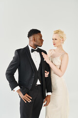 A beautiful blonde bride in a wedding dress and an African American groom in a tuxedo standing side by side.