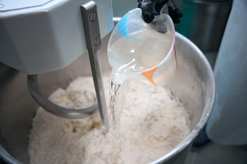 Chef pours water into a dough kneading machine