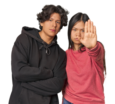 Young interracial couple in studio standing with outstretched hand showing stop sign, preventing you.