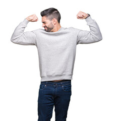 Young handsome man wearing sweatshirt over isolated background showing arms muscles smiling proud. Fitness concept.