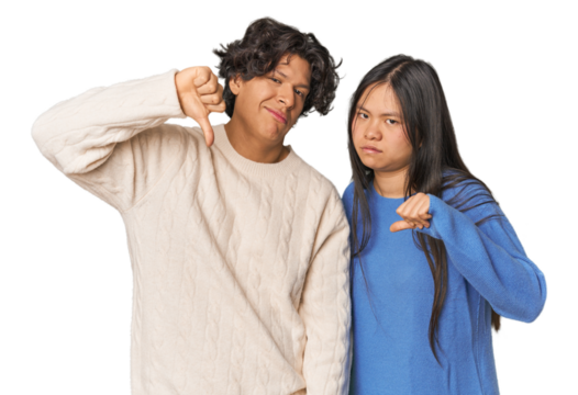Young interracial couple in studio showing thumb down, disappointment concept.
