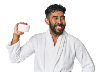 Hispanic male with moisturizer in studio looks aside smiling, cheerful and pleasant.