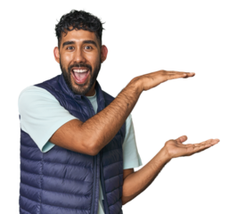 Young Hispanic man isolated shocked and amazed holding a copy space between hands.