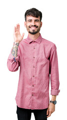Young handsome man wearing pink shirt over isolated background Waiving saying hello happy and smiling, friendly welcome gesture © Krakenimages.com