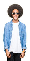Young african american man with afro hair wearing thug life glasses with a happy and cool smile on...