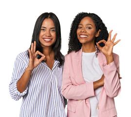 Young Latin businesswomen in studio winks an eye and holds an okay gesture with hand.