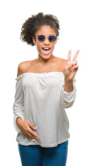 Young afro american woman wearing sunglasses over isolated background smiling with happy face winking at the camera doing victory sign. Number two.