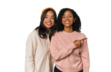 Young Latin friends together in studio smiling and pointing aside, showing something at blank space.