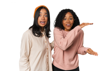 Young Latin friends together in studio shocked and amazed holding a copy space between hands.