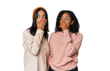 Young Latin friends together in studio thoughtful looking to a copy space covering mouth with hand.