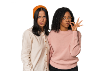 Young Latin friends together in studio with fingers on lips keeping a secret.