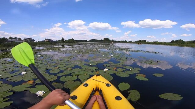 Kayaking along river through growing white lily nymph on sunny summer day. Person floating in boat on river with surface of water reflecting white clouds on calm day. Tourism. Active lifestyle. POV