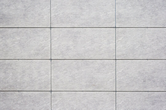 Close up of a tiled wall with a grid pattern, featuring light gray tiles and dark grout lines, as texture, background.