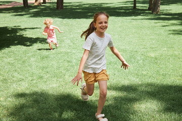 Fototapeta premium Happy Caucasian laughing kids sisters running on the grass on hill in park enjoying active rest together on summer holiday sending time on weekend