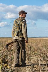 Mature man hunter with gun while walking on field.