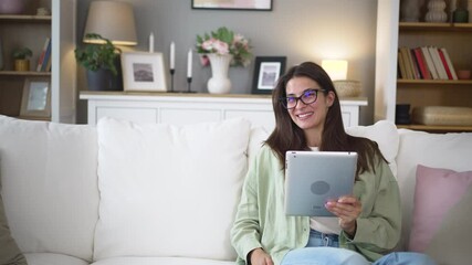 Attractive woman, freelancer holding and using digital tablet, sitting at cozy sofa in living room. Successful businesswoman text message in home. Online technology concept, remote job and work.