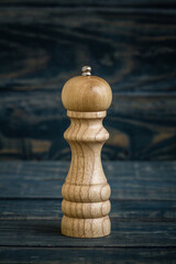 Wooden pepper mill placed on a dark blue wooden surface.