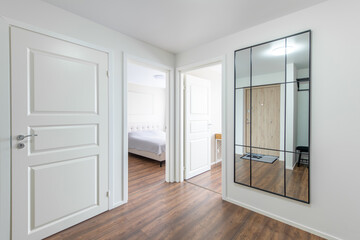Home Entrance Hall. Interior. Wooden White Door, Brown Flooring and White Wardrobe. Minimalism. LED Light. Open Doors to Bedroom and Living Room