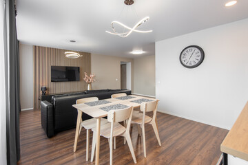 Modern Home Living Room and Kitchen Interior. Luxurious Stylish Modern Apartment. Open Space, Stylish Black Leather Sofa, White Furniture, Scandinavian Design. Cllock on the Wall, TV Screen