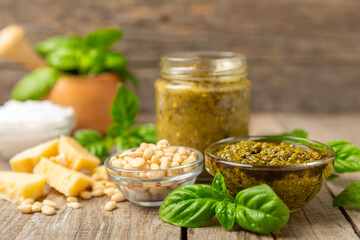 Pesto. Italian basil pesto sauce on a textured wooden background. Ingredient for pesto sauce: fresh basil, pine nuts, Parmesan cheese and olive oil. Space for text.Copy space.