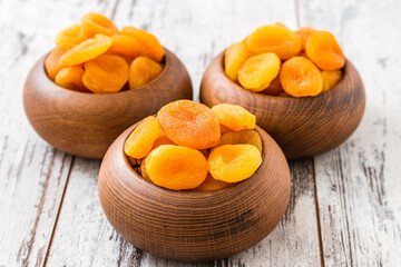 Dried apricots in wooden bowls on a rustic white wooden table, the bright orange color of the apricots contrasting with the natural brown of the bowls.