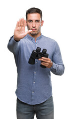 Handsome young man looking through binoculars with open hand doing stop sign with serious and confident expression, defense gesture