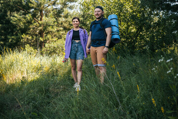 Fototapeta premium Happy couple tourists with backpacks walking outdoors in the summer forest