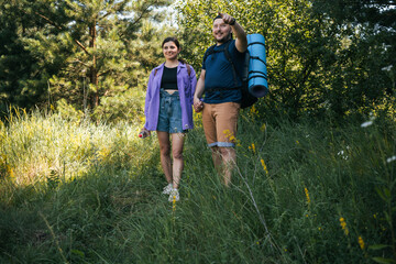 Fototapeta premium Happy couple tourists with backpacks walking outdoors in the summer forest