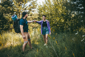 Fototapeta premium Happy couple tourists with backpacks walking outdoors in the summer forest