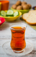 Glass of tea on a saucer, with bowls of cucumbers and bread in the background on a white wooden table.