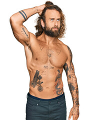 Fototapeta premium Handsome man with beard and long hair standing shirtless showing tattoos confuse and wondering about question. uncertain with doubt, thinking with hand on head. pensive concept.